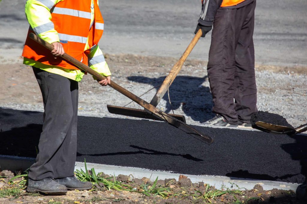 Crew raking hot-mix asphalt on a new edge