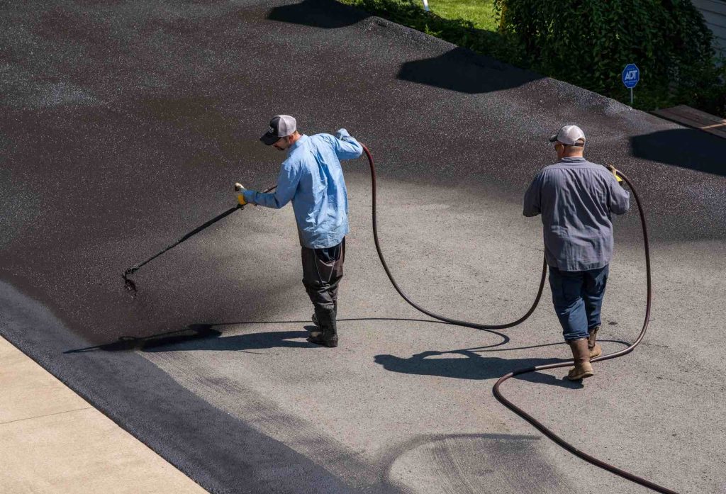Crew spray-applying sealcoat to a driveway